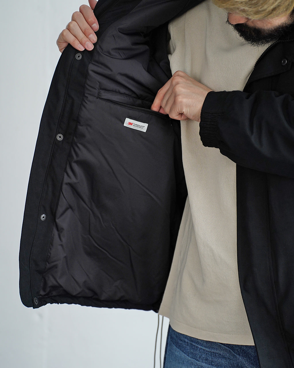 Baggies Jacket Ver.2 の内側ポケット付きジップポケットを持つ着用イメージ。黒系の裏地と前立てを開いた様子を捉え、3M THINSULATE中綿の保温性を示唆する構造が分かる写真。