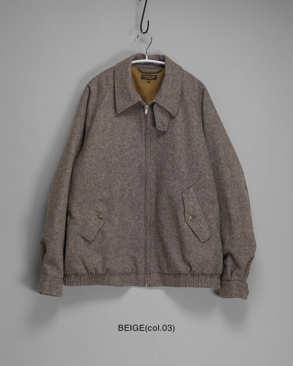 Harrington Jacketのベージュ系ツイード生地、前開きファスナーとポケットが特徴的なフロント。襟元は立ち上がるスタンドカラー仕様の2WAYで調整可能
