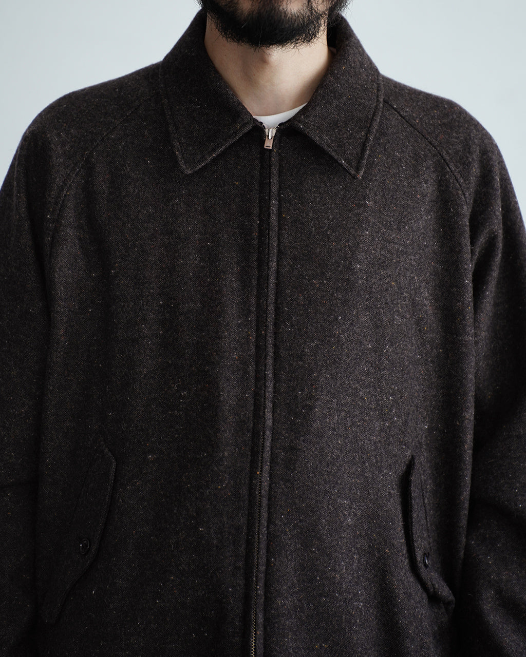 ダークセピアの Harrington ジャケット。前中心のジッパーと2WAY襟でスタンドカラーとしても着用可能なデザイン。ポケット口は斜めフラップタイプ、布地は杢調のウール混素材の質感が伝わる正面ショット。