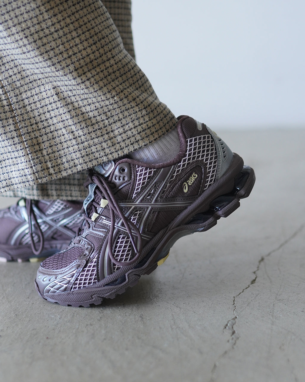 淡いパープルとグレーのアシックス GEL-NIMBUS 10.1、アッパーのオープンメッシュと丈夫なパーツ使いが特徴のランニングシューズ。足元のディテールが立体感を演出する着用イメージ。