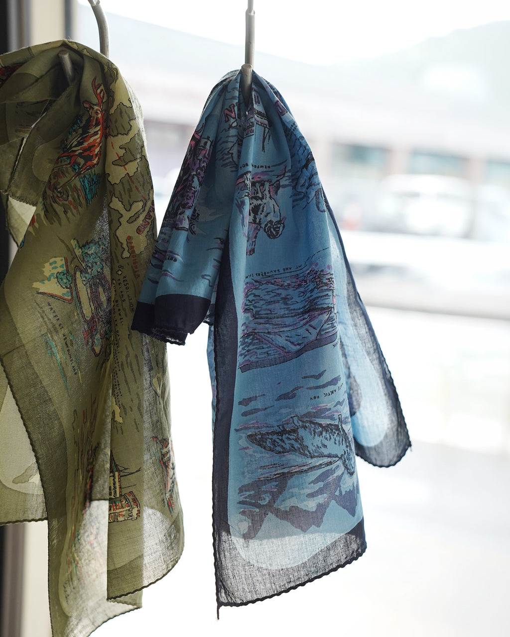 グリーン系とブルー系の模様が入った50×50cmのバンダナ風ストール。薄手で透け感があり、端を黒い縁取りで仕上げたデザインが特徴です。