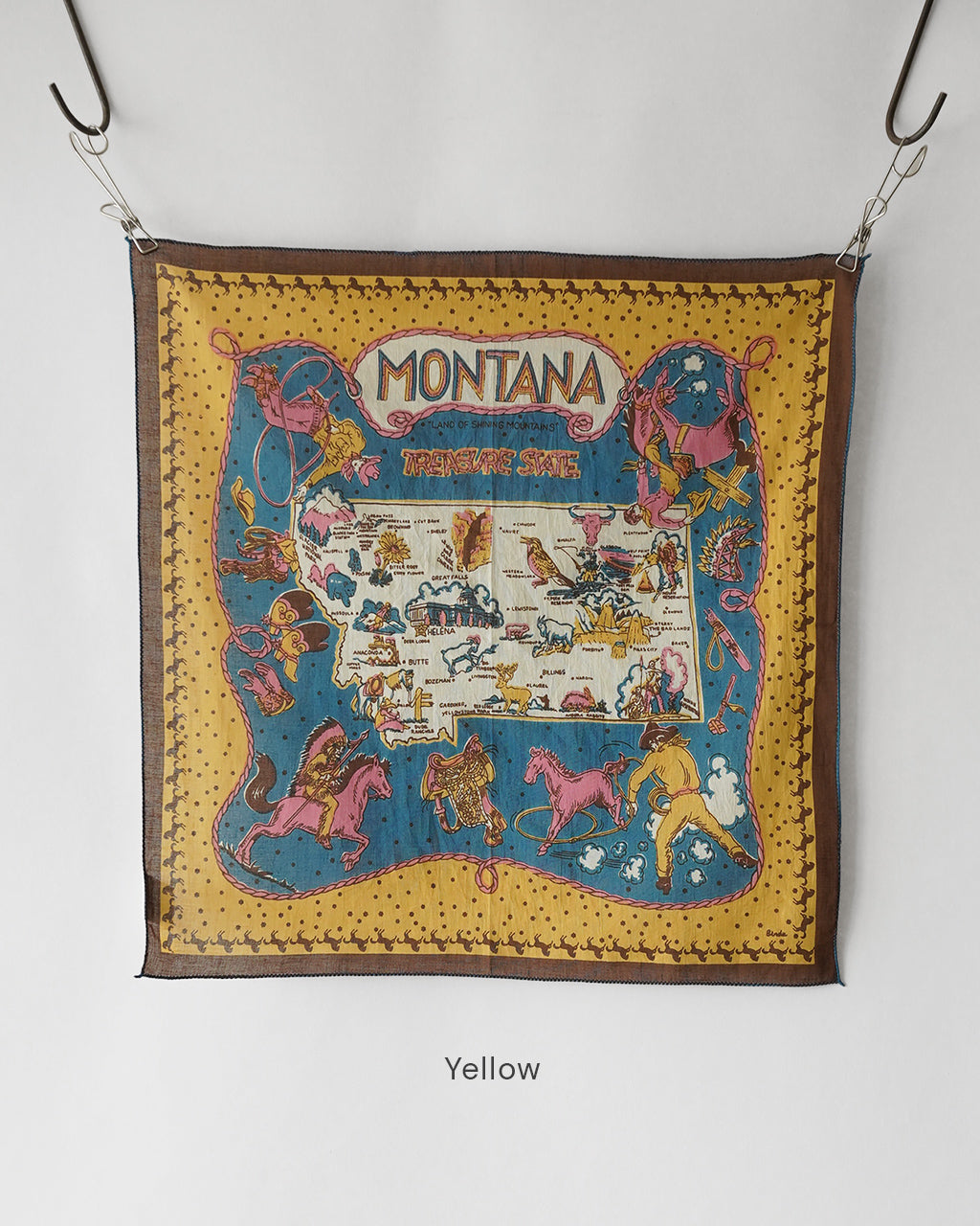 Montana柄の50×50cmスカーフ状の広幅布。黄色地に周囲のボーダーと馬や人物のイラストがプリントされ、吊り下げ金具が見える装着可能な状態で写っています。