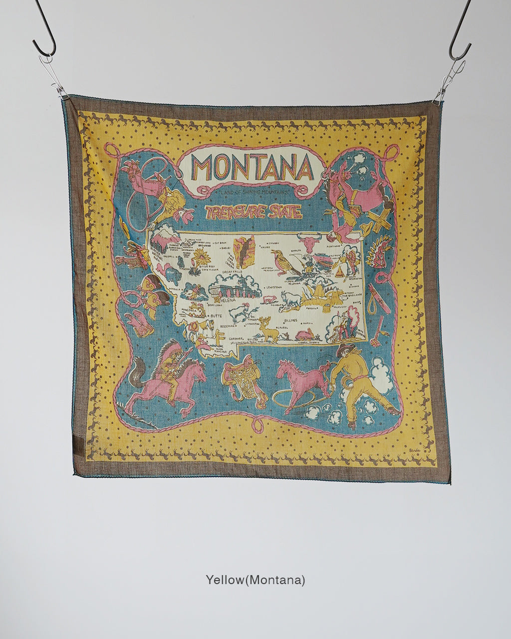 Montana柄の黄地に馬や人が描かれた大判スカーフ。中央には地図風モチーフが入り、周囲を黄色の縁が縁取るデザインです。