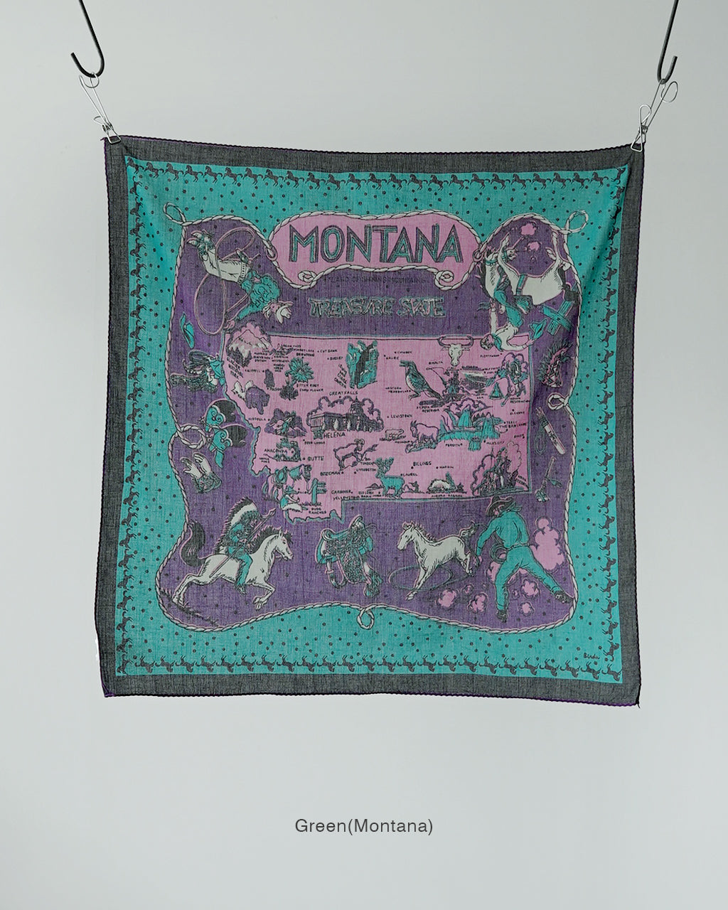 Montana の文字が中央に配されたターコイズとパープルの大判スカーフ。両端に金具付きの吊り下げヒモが見え、全体に動きのあるデザインが印象的。