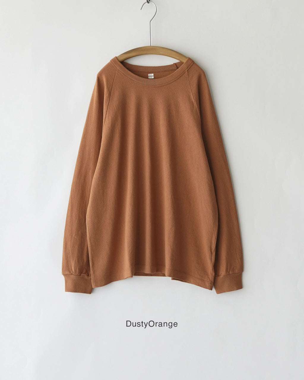 コットンとシルク混紡のラグランTシャツ、アイボリー系ではなくダスティオレンジ色の長袖。生地表面にネップ感とムラがあり、肩のラインは落ち着いた印象。