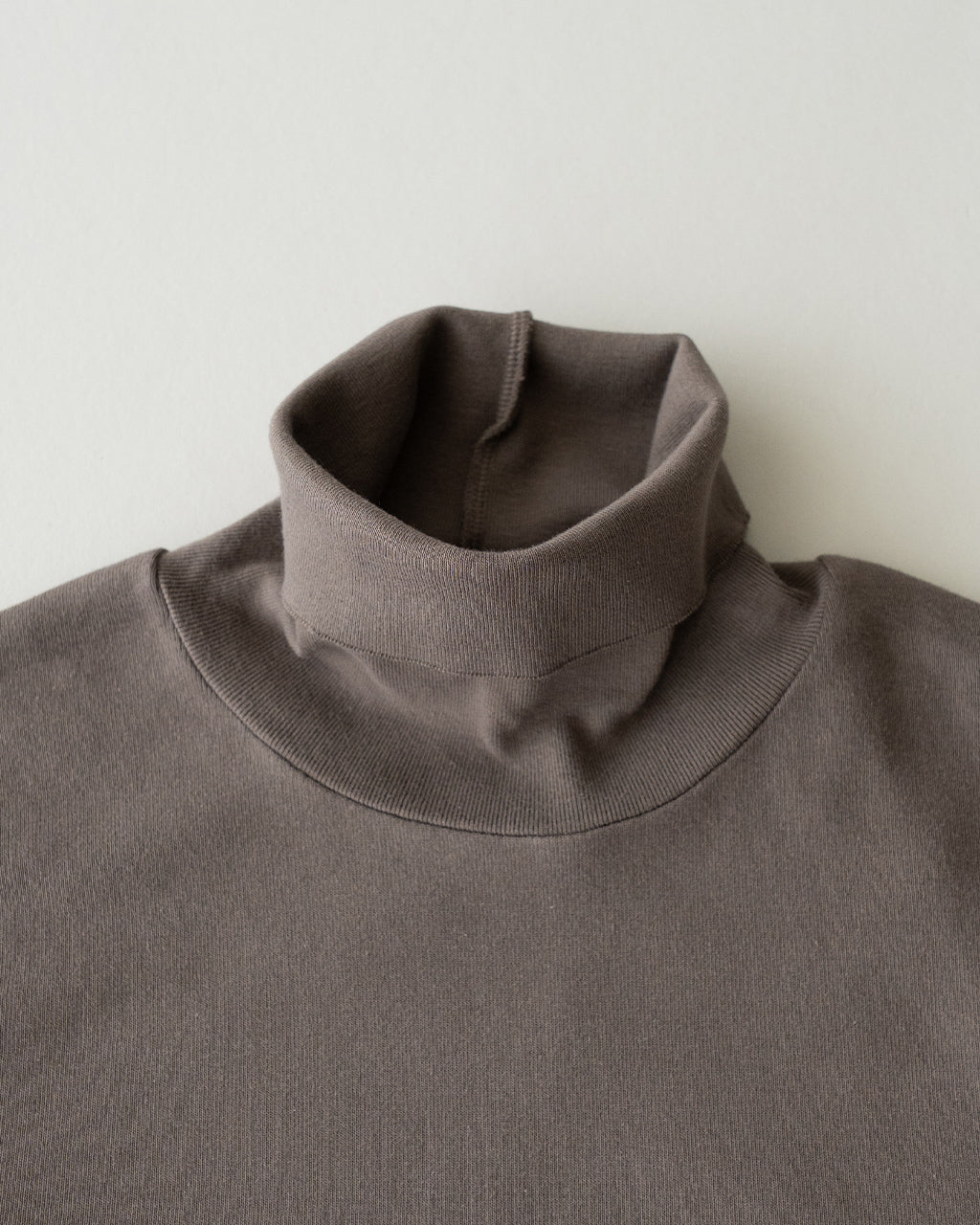 タートルネックのリブ編み長袖Tシャツ。落ち着いたダークグレーカラーで首元をすっきり包み込むデザインがアップで写っています。
