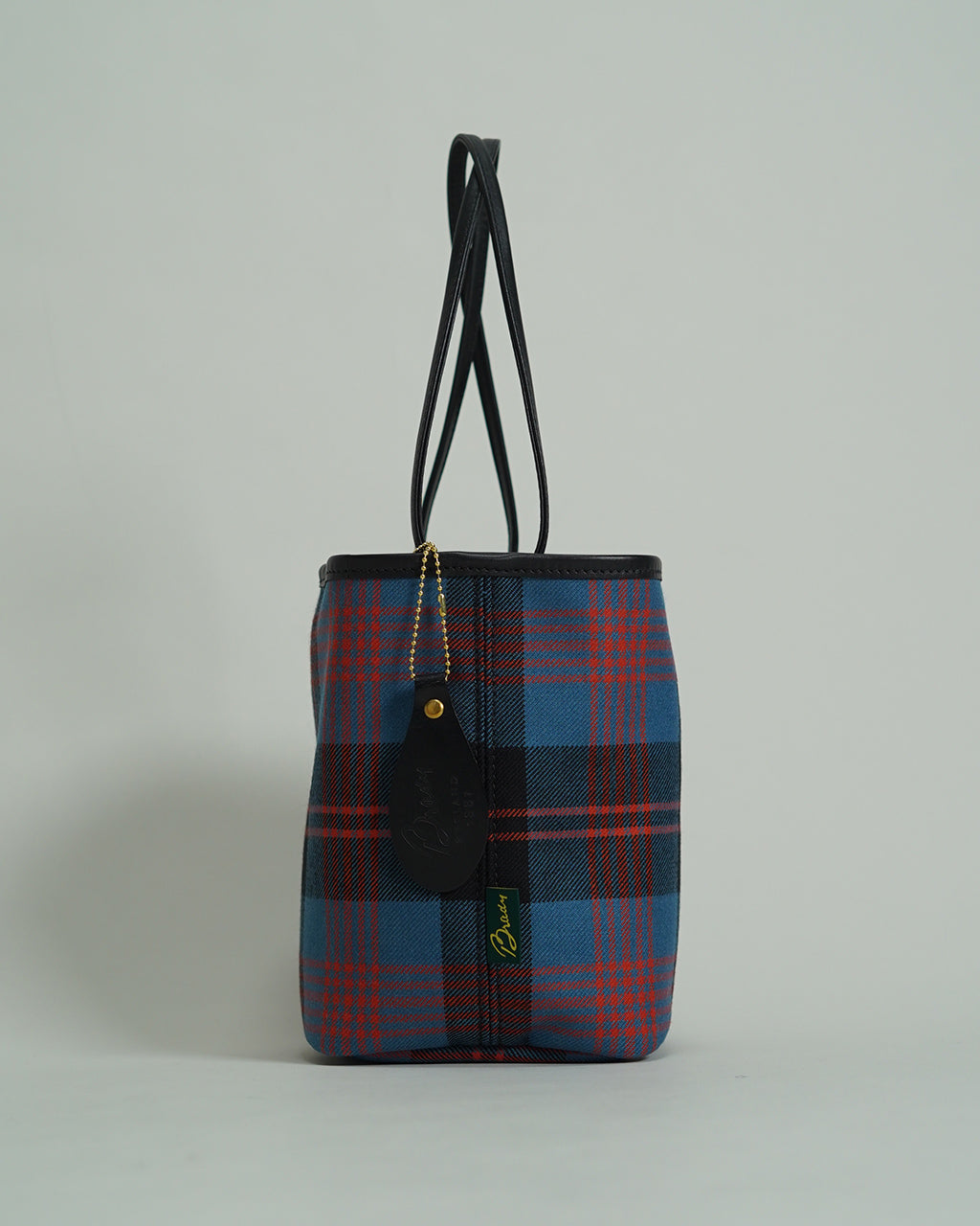 ブレディのKEER LOCHCARRON WOOL CHECK。赤と青のタータンチェックが全面に入った巾着型ショルダーバッグ。黒のレザーハンドルと金属チェーンのタグがアクセントとして垂れるデザイン。