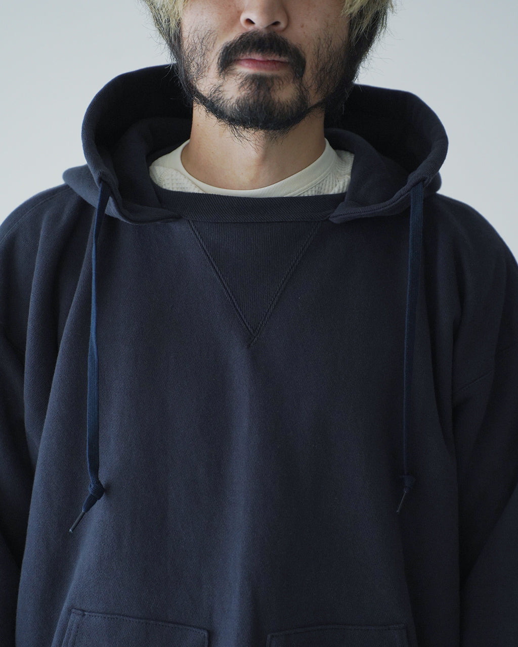 ネイビーのフード付きスウェットパーカー。前方には大きめのフードとヒモ、胸元にはV字ステッチが特徴的で、肩のラインがゆったりとしたリラックスシルエット。