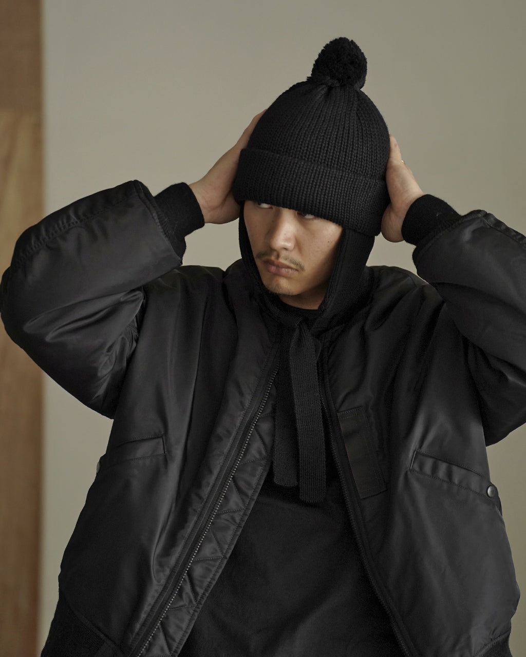 黒い耳付きニット帽を男性が両手で位置を整えて着用している