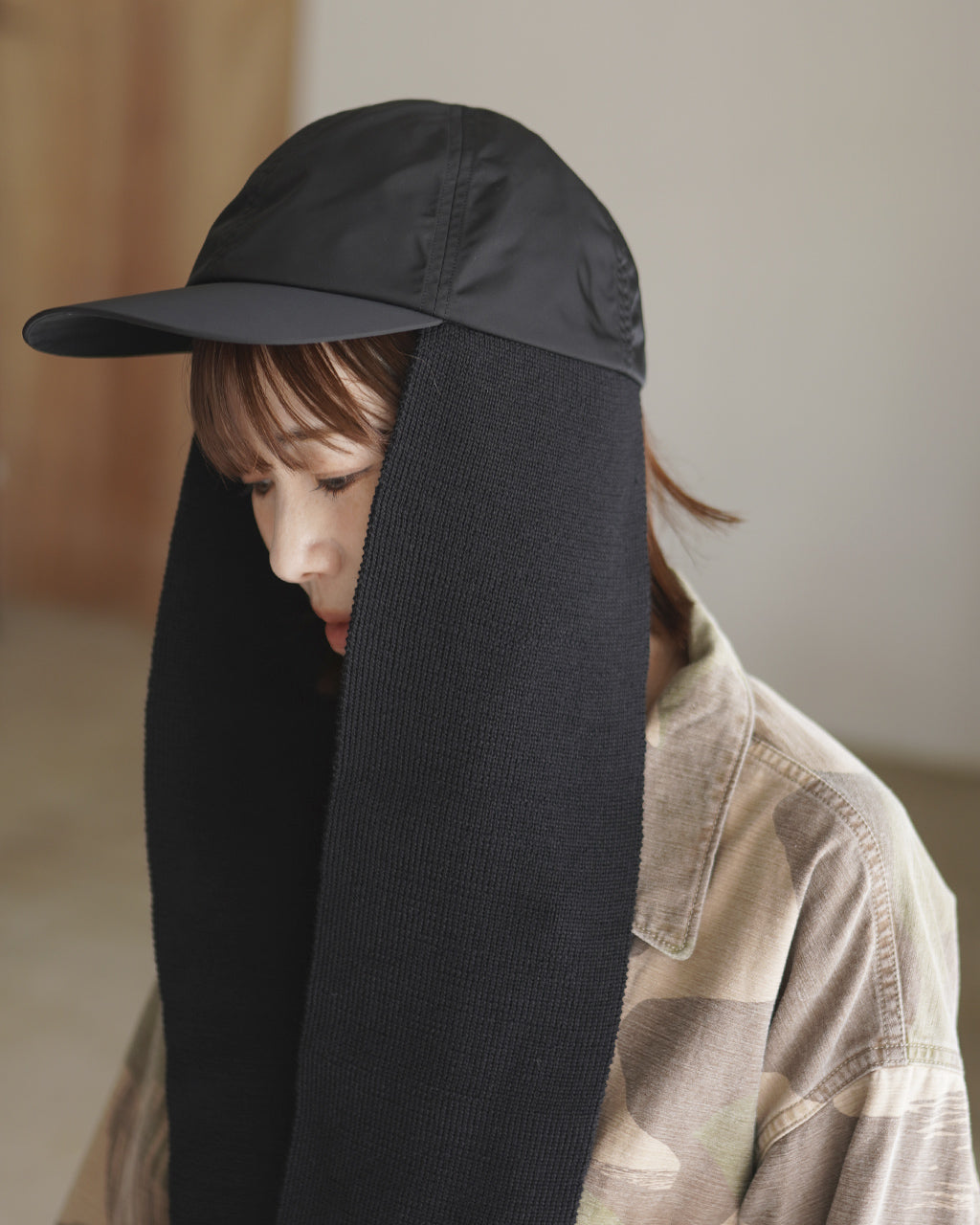 黒のマフラー部分が縦に大きく垂れた着用写真。キャップのつばが上に出て、内側の落ち着いた編み目が見える