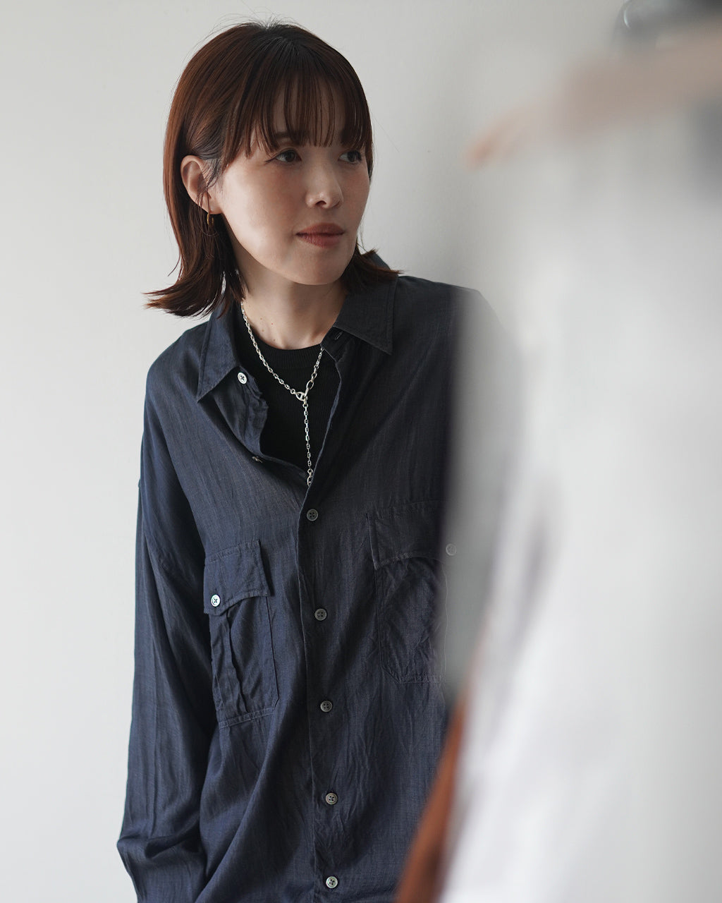 ブラックのシャツを着た女性が前方を見据える姿。ネックレスは細身のチェーンと大ぶりのアンカーで、胸元にさりげなく垂れるデザイン。