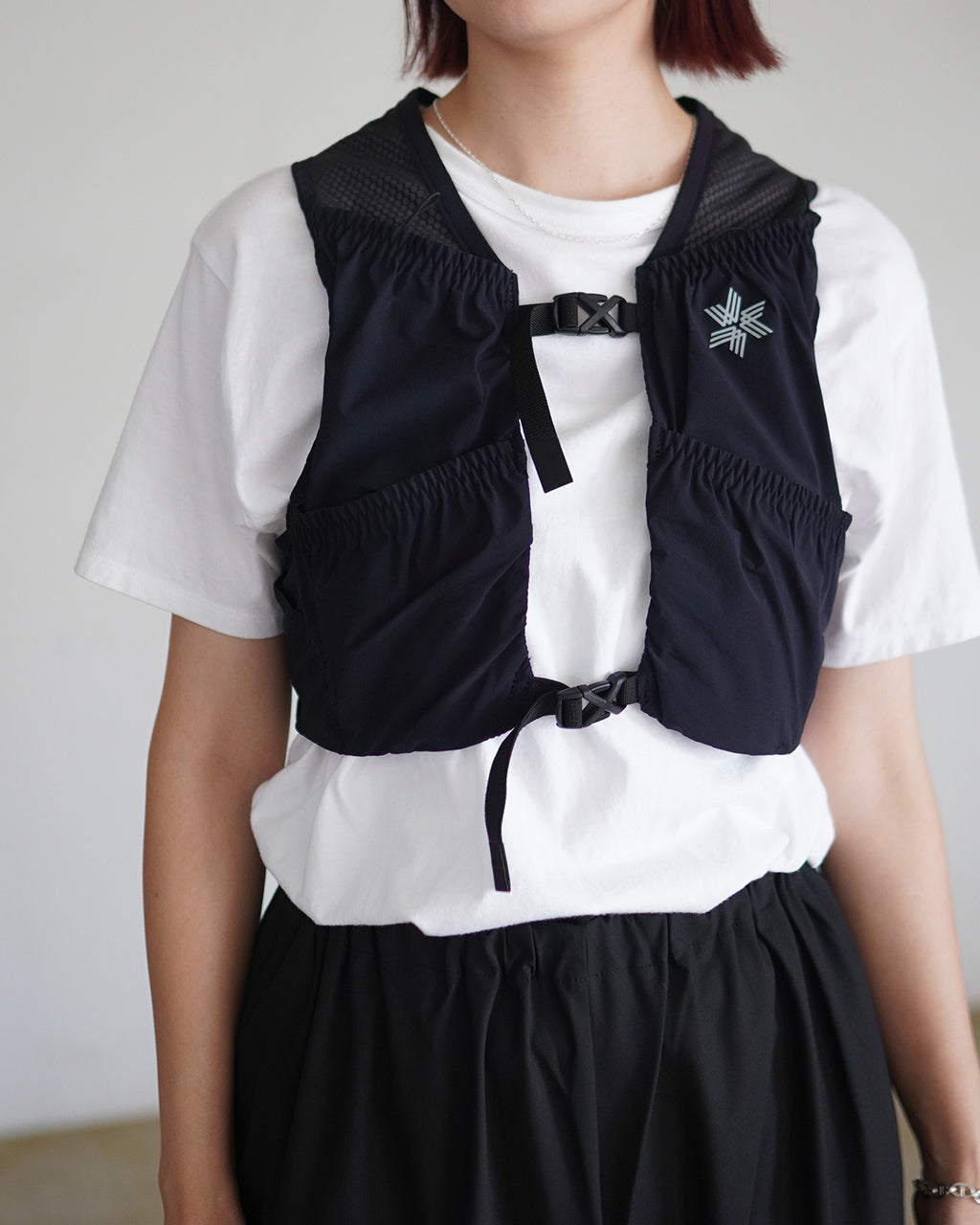 ブラックのベストを前から着用した女性の上半身、白いTシャツの上に重ね、胸元の留め具と前開きのデザインが映える様子