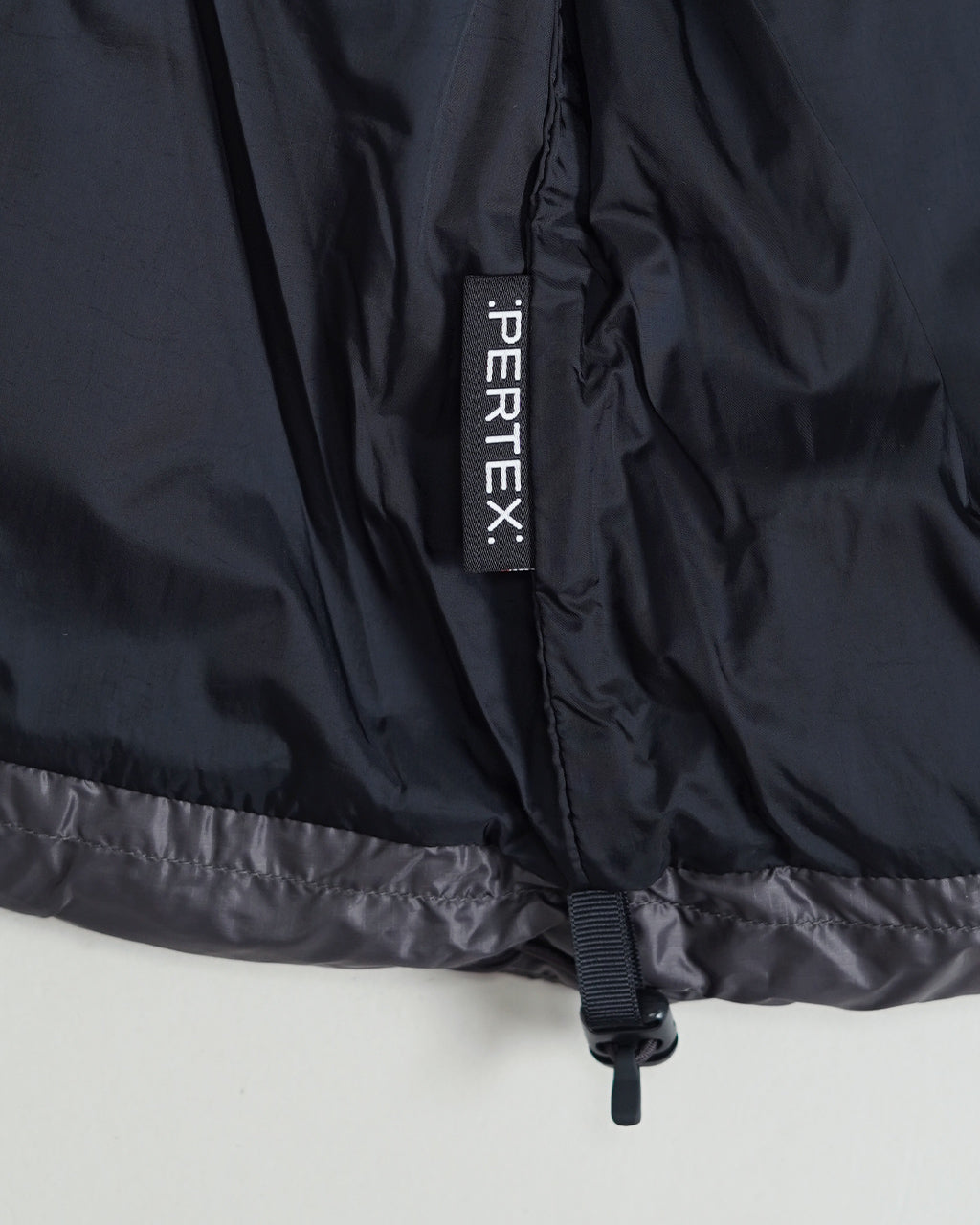 ブラック系の裏地とドローストリングが見えるダウンパーカの裾部分。縦長のブランドタグ“PERTE X”が目を引くディテールショット