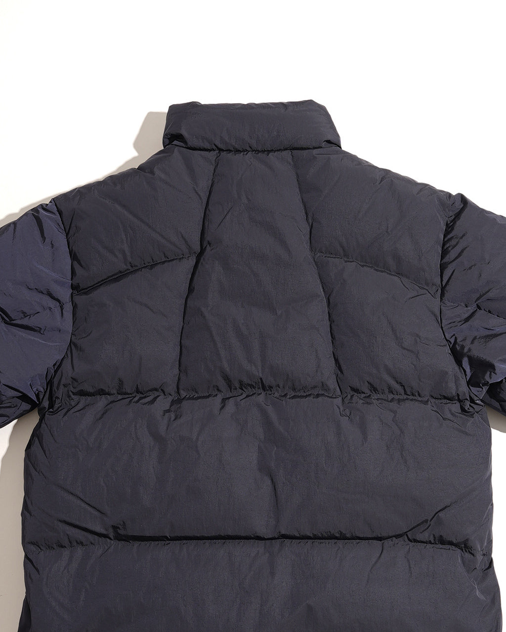 背中から見たゴールドウインのDope Dyed Ripple Nylon Down Jacket。ディープネイビー系の陰影と立体的なキルティング、肩回りのボリューム感が特徴的です。