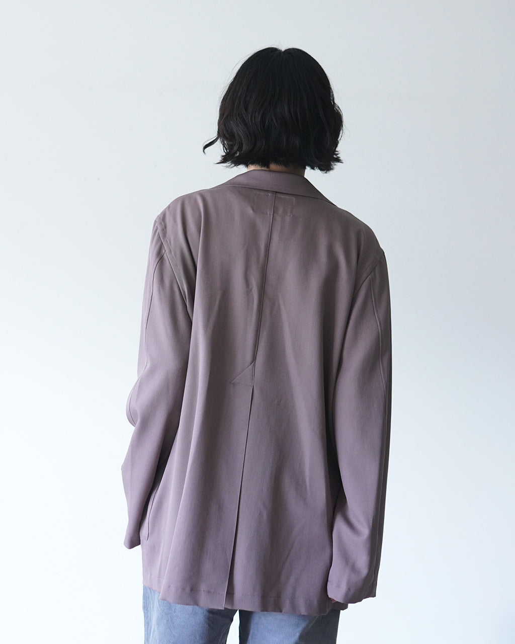 背面から見たモーブカラーのジャケット。ゆったりとしたシルエットで、肩幅と着丈が程よく落ち着いた印象。後ろ中心の縫い目がアクセントになっている