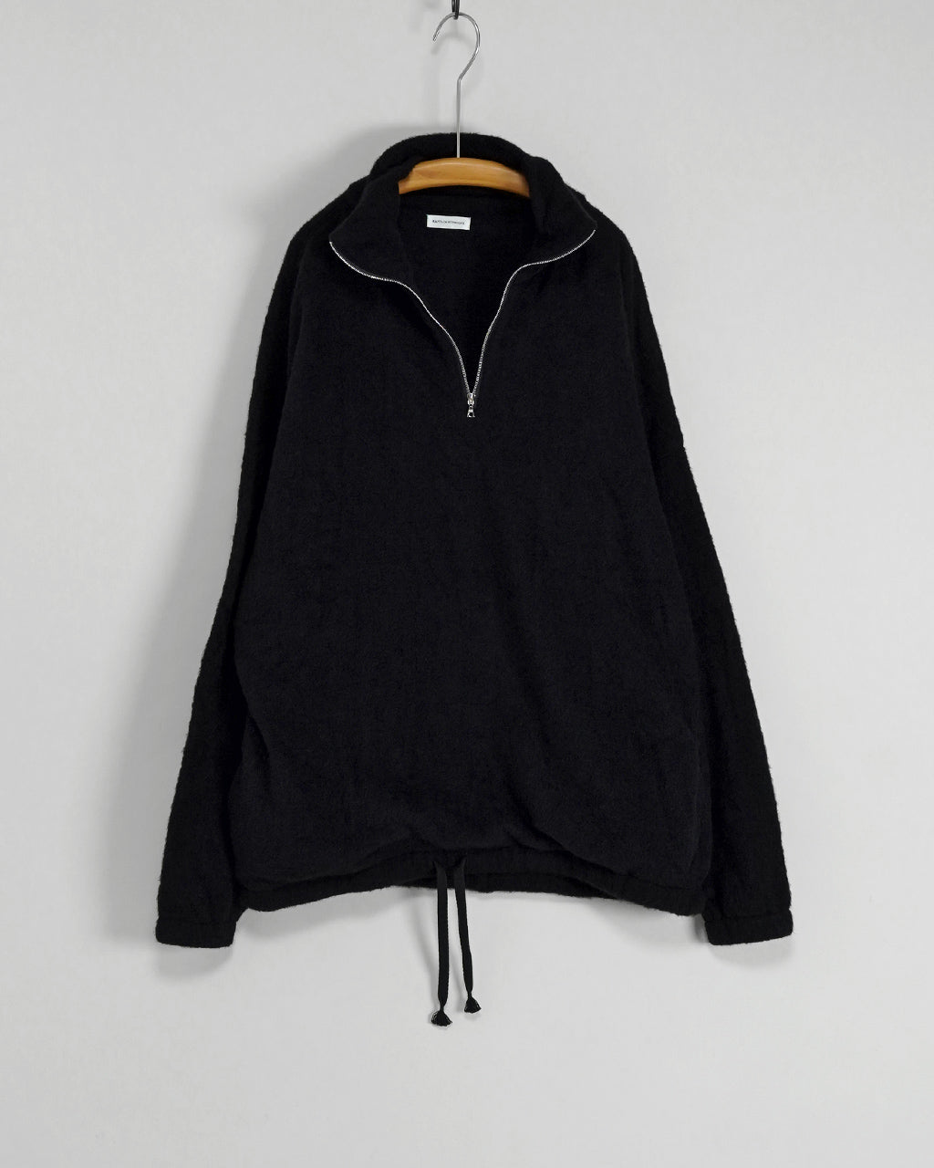 前面が大きく開くジッパー付きの黒いフリース pullover。スタンドカラーと裾のドローコードが特徴で、肩のラインに沿うゆったりとしたシルエットが確認できる