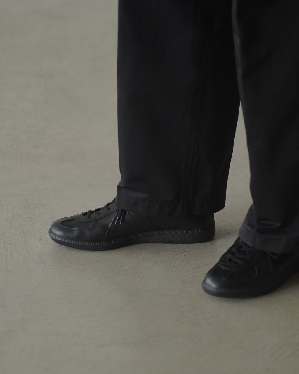 カウレザーのアッパーを用いた Unlined KS Trainer の着用イメージ。黒系のパンツと合わせた足元のアップで、ソールはラバー製のシンプルなデザインです。