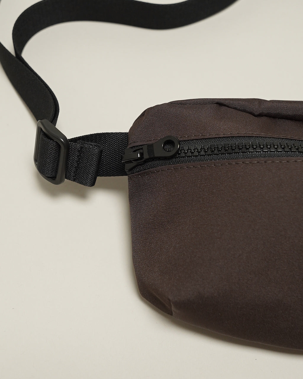 KARRI AMIACALVAのウエストバッグ。茶系の生地に黒いジッパーとストラップを組み合わせたディテールショット。腰周りに沿うコンパクトな形状とベルト部の留め具が見える。
