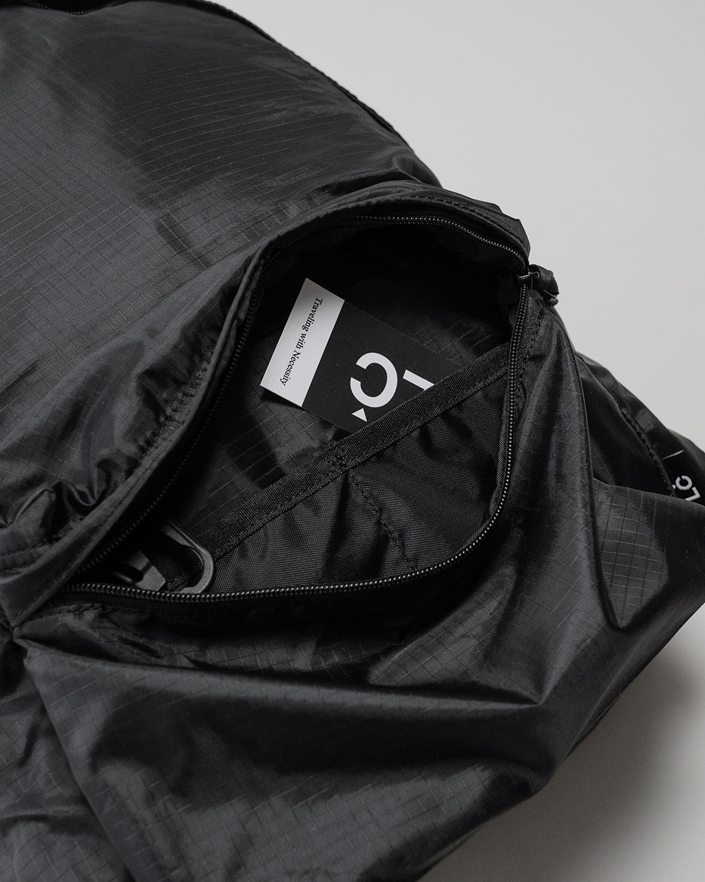 LC by LOWERCASEのDAYPACK LITE 20Lの正面を開いた状態。軽量ナイロン生地とファスナー開閉部、内部にタグが見える。ブラック系の色調で実用的なデザインが窺える
