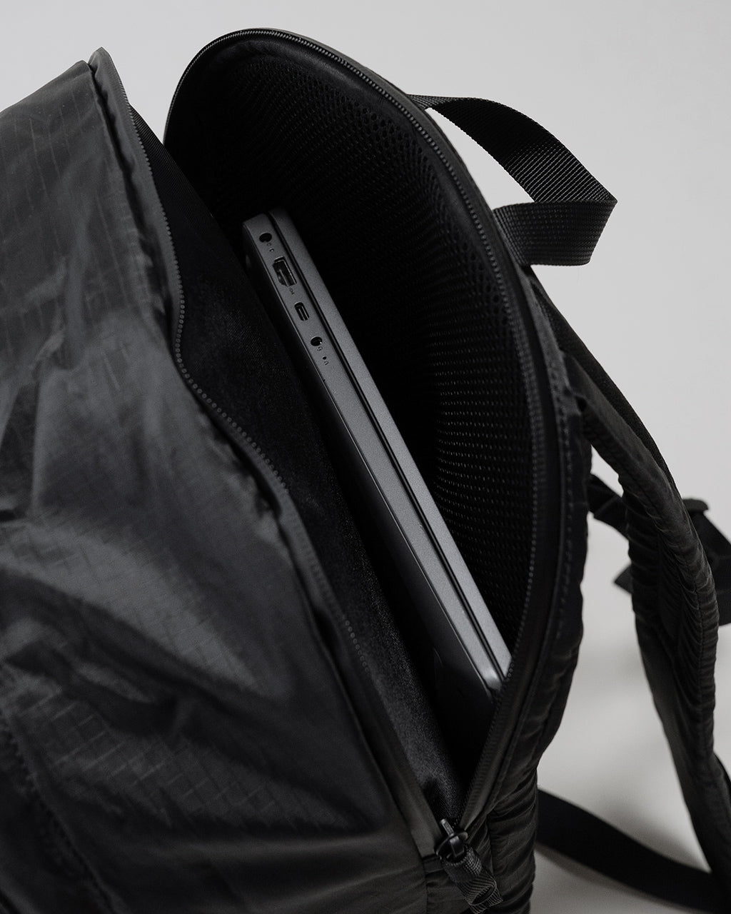 LC by LOWERCASEの DAYPACK LITE 20Lの側面とファスナー周りをアップで捉えたブラック系リュックの内部構造。薄型ノートPCが収納できるポケットの様子が見える。