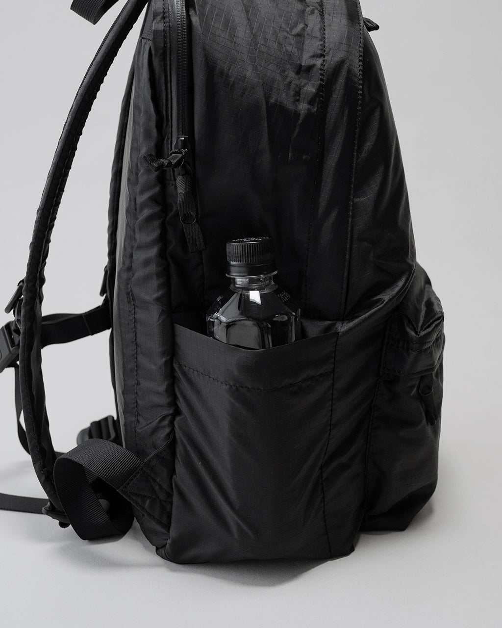 LC by LOWERCASEの DAYPACK LITE 20Lの側面ポケットにボトルを収納したブラック系のバックパック画像