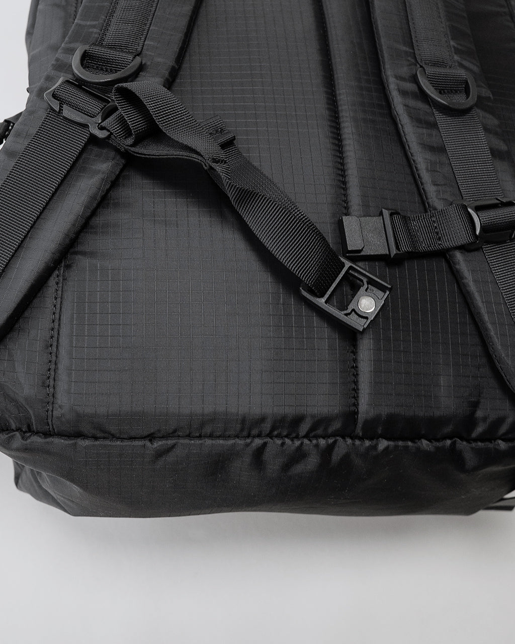 LC by LOWERCASEのDAYPACK LITE 30Lの背面寄りのショット。黒系生地に細かな格子模様と、胸元のストラップ金具とバックルのディテールが鮮明に映る写真。