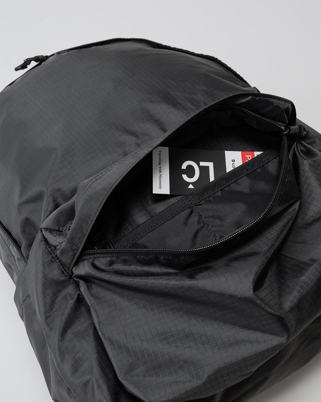 LC by LOWERCASEの DAYPACK LITE 30L黒系の開閉部アップ。ジッパー付きの収納口と内部タグが見える、軽量感のあるナイロン生地のバックパック正面ショット。