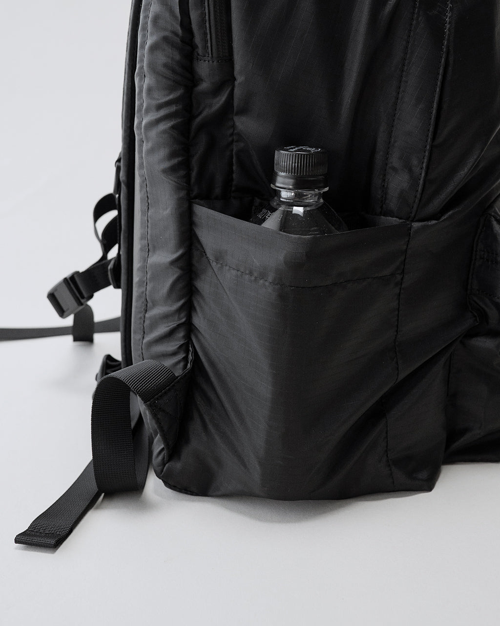 黒のLC DAYPACK LITE 30Lのサイドポケットにボトルを収納した状態。背面部分と縫製が見え、軽量なナイロン素材の質感が伝わる写真