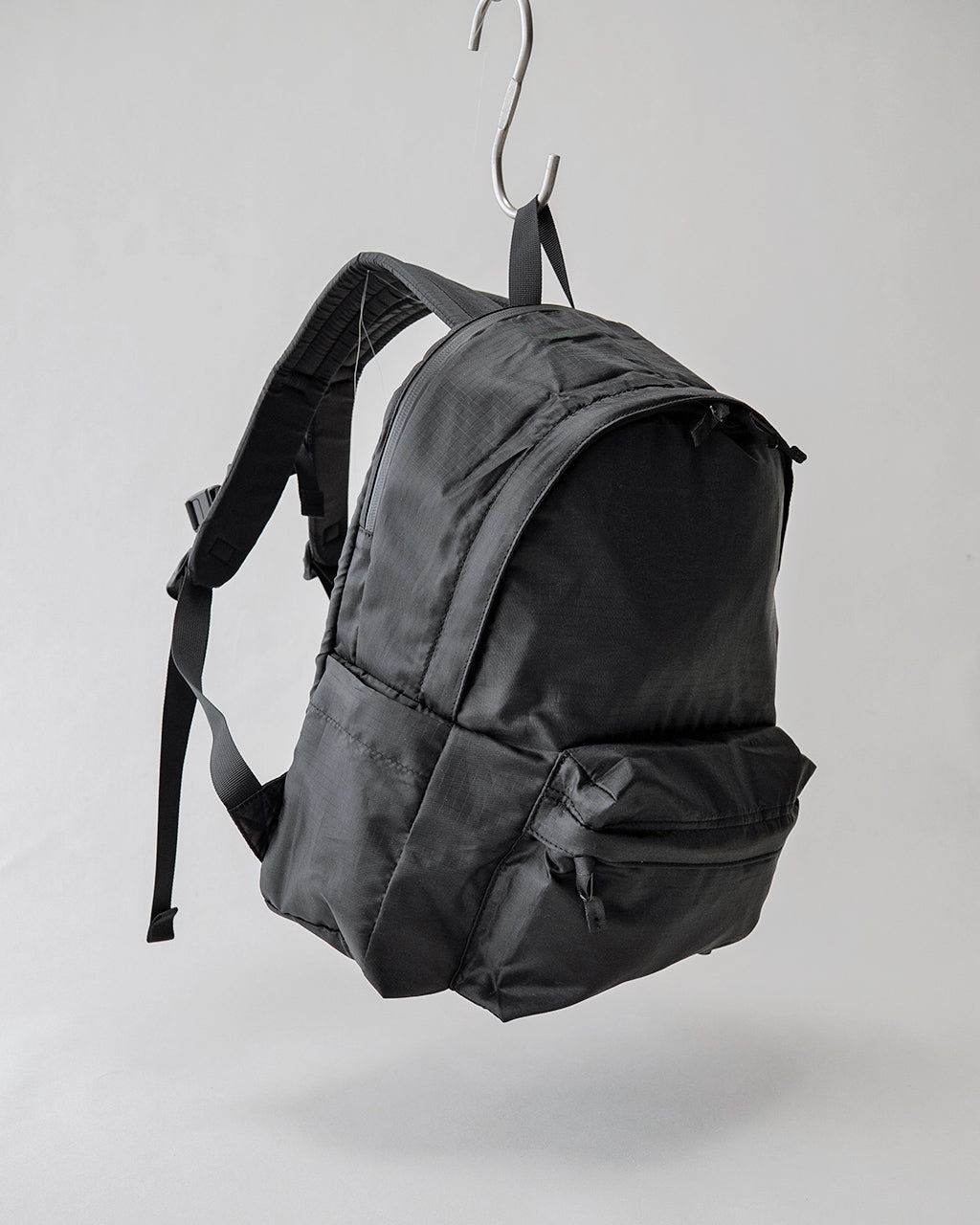 LC by LOWERCASEの DAYPACK LITE 16L。黒系のバックパックを吊り下げた全体像で、前面ポケットとサイドの縫い目が見える。軽量ナイロン素材の質感が伝わる写真。