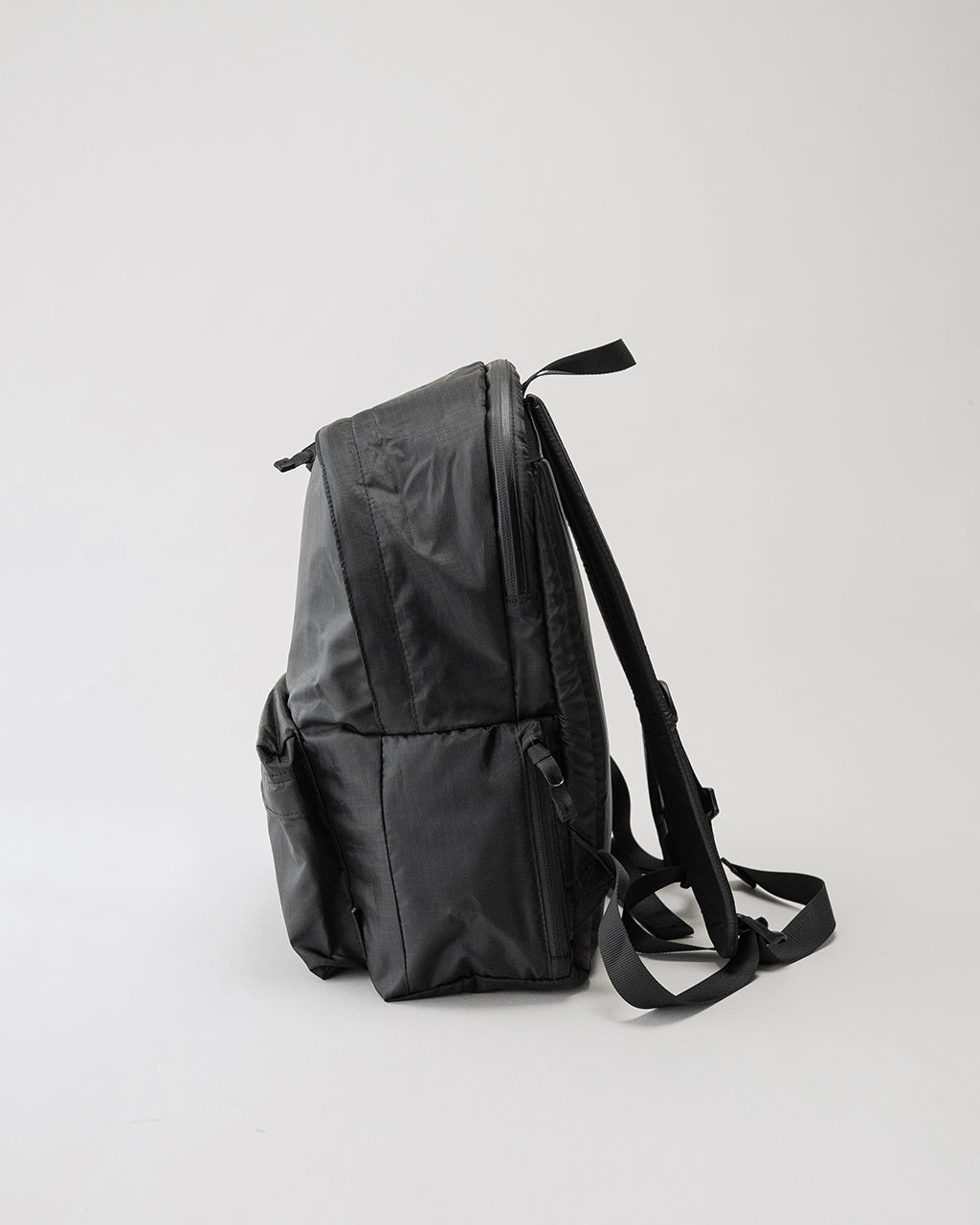 LC by LOWERCASE の DAYPACK LITE 16Lのサイドから見た黒系バックパック。薄手ナイロン素材で、メイン収納のファスナーとショルダーストラップが視認できる。