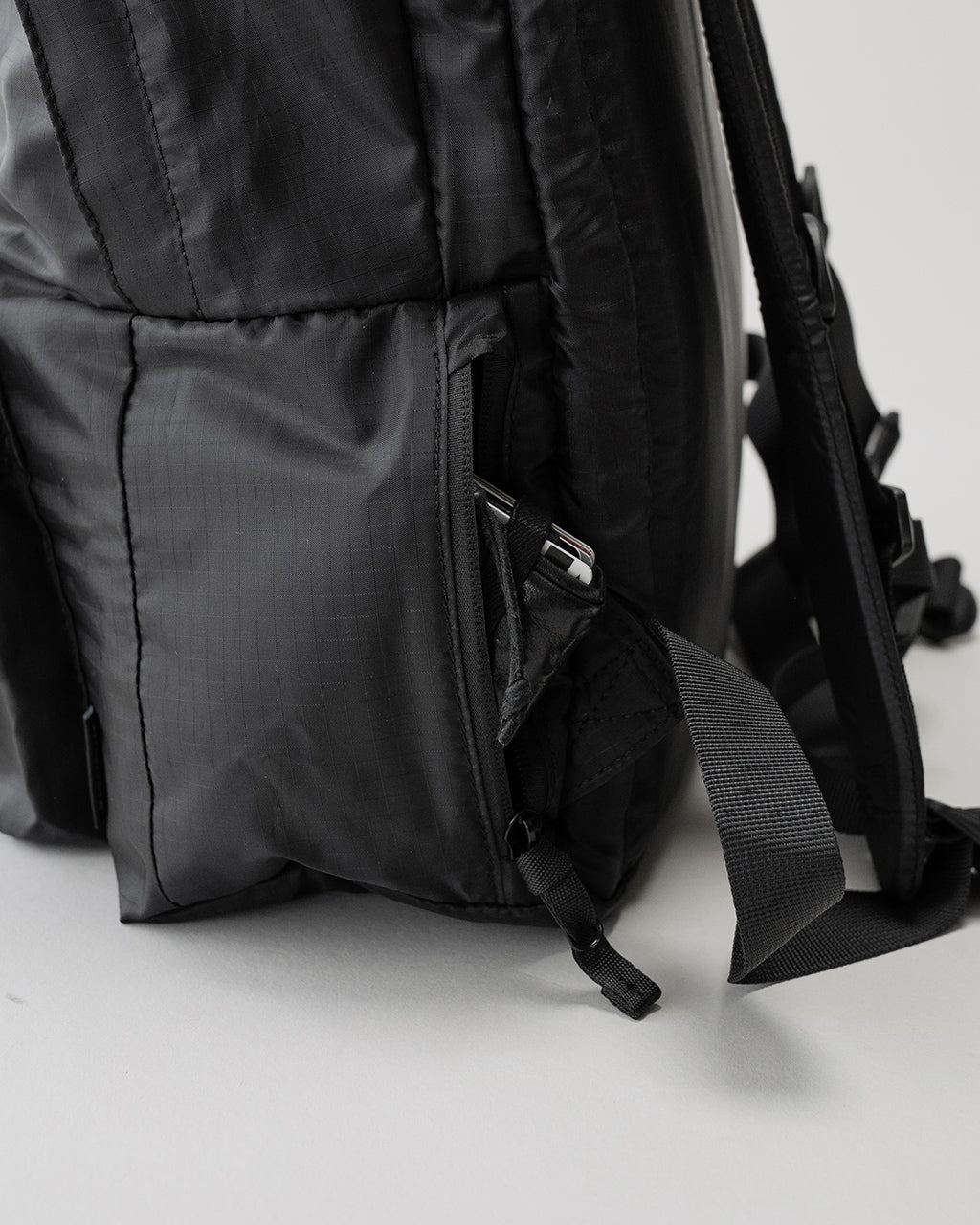LC by LOWERCASE の DAYPACK LITE 16L の側面。黒色の薄手リップストップ生地とサイドポケット、調整ストラップが見えるディテール画像