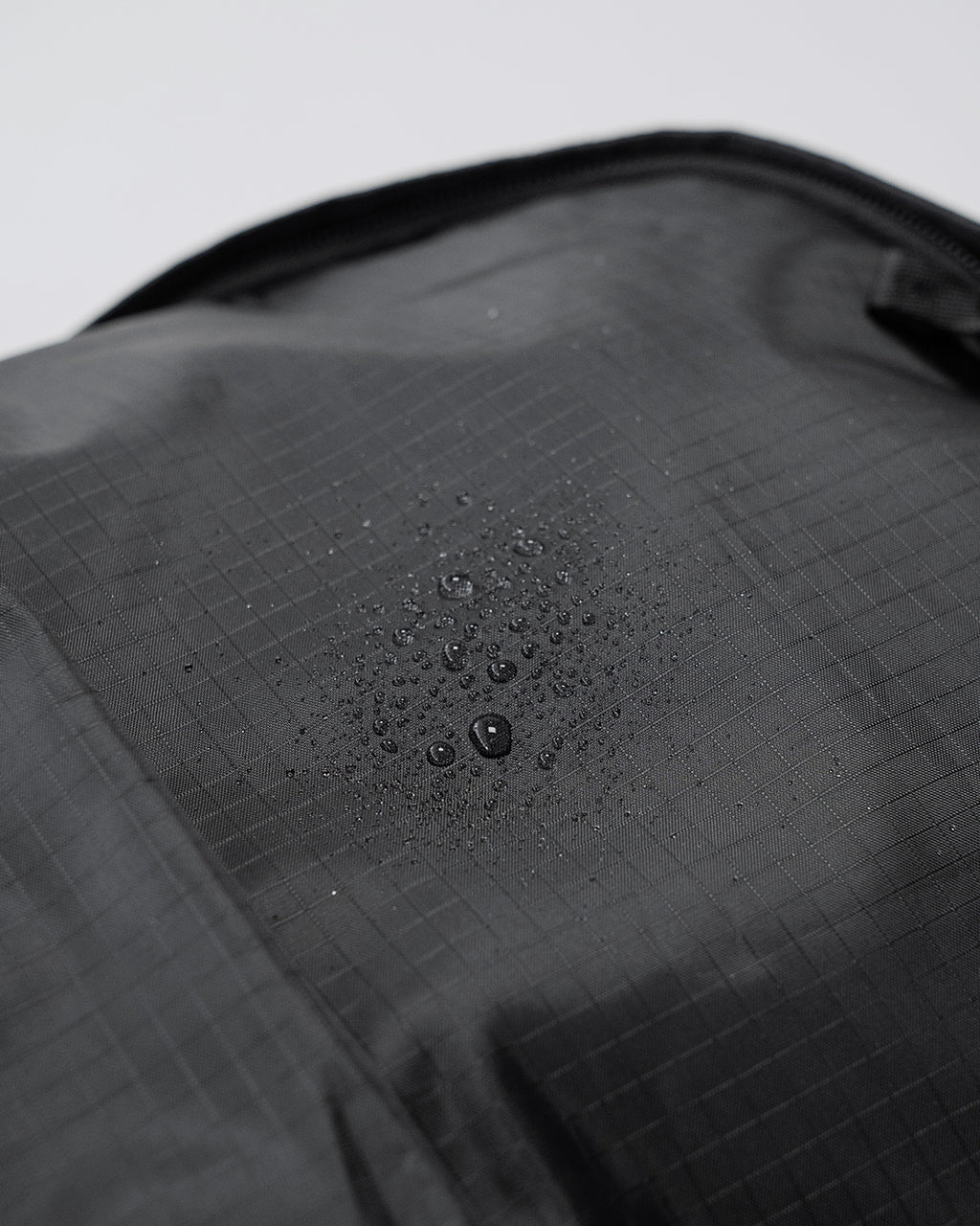LC by LOWERCASE の DAYPACK LITE 16L。黒系素材の表地に格子状の柄が施され、撥水加工のような水滴が表面にとどまるディテールが分かる背中部分寄りのアップショット