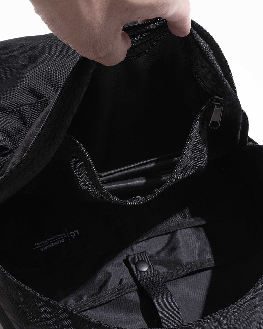 ブラックの DAYPACK Msize 内部のPCスリーブと仕切りポケットが見える、開口部を指で押さえた状態の写真