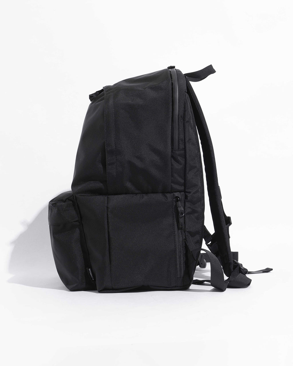 ブラックの DAYPACK Lsize の横からのシルエット。背負い紐と側面ポケットが見えるサイドショット。