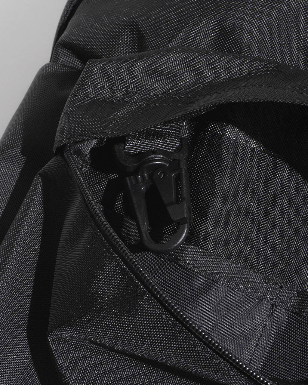 ブラックの DAYPACK Lsize のジッパー周りをアップで捉えたディテール写真。丈夫なナイロン織りと繊細な質感が際立つデザインで、外ポケットのファスナー部とコーナー部分の縫製が見える。