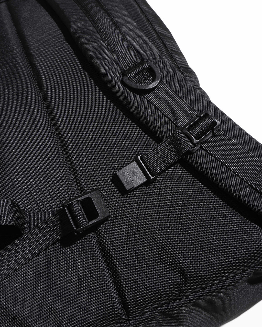 ブラックのDAYPACK Lsizeのショルダーストラップとバックル部分のアップ。高強度ナイロン生地とダブルファスナー周りの細部が見えるディテールショット。