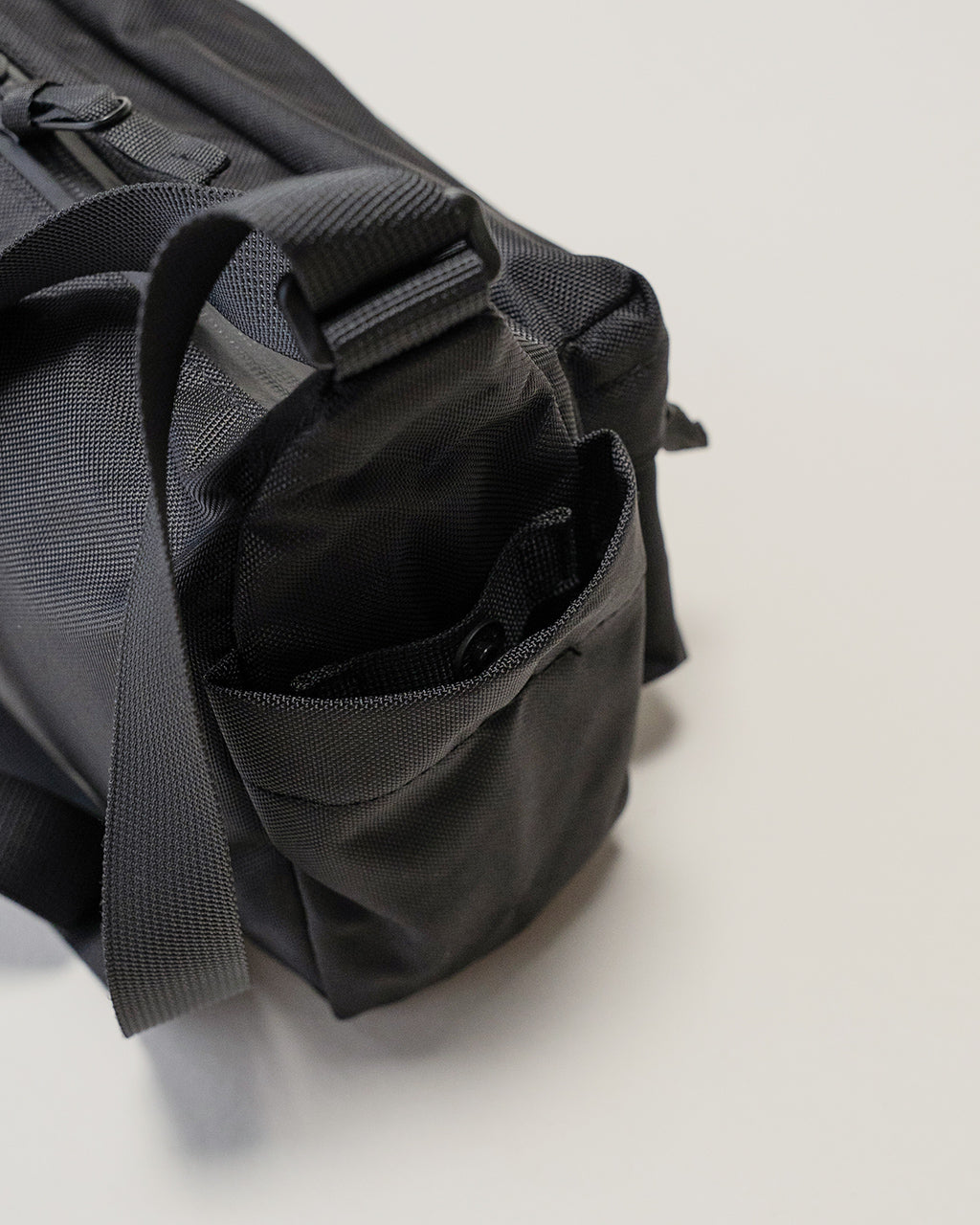ブラックの小型ショルダーバッグ。側面ポケットと前部ジップポケットを備え、耐久性のあるナイロン素材の質感がわかるショット。