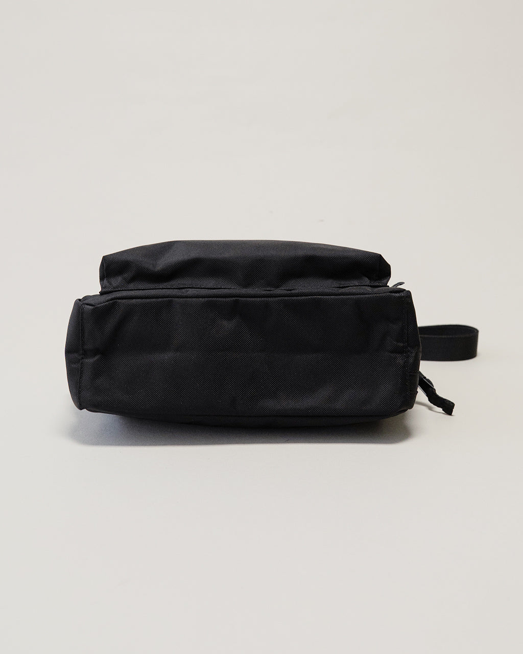 LC by LOWERCASEのブラック系ショルダーバッグ。底面を横から見た薄型で、前後にポケットなしのシンプルなフォルム。素材は耐久性のあるナイロンの光沢感が控えめに映えるデザイン。