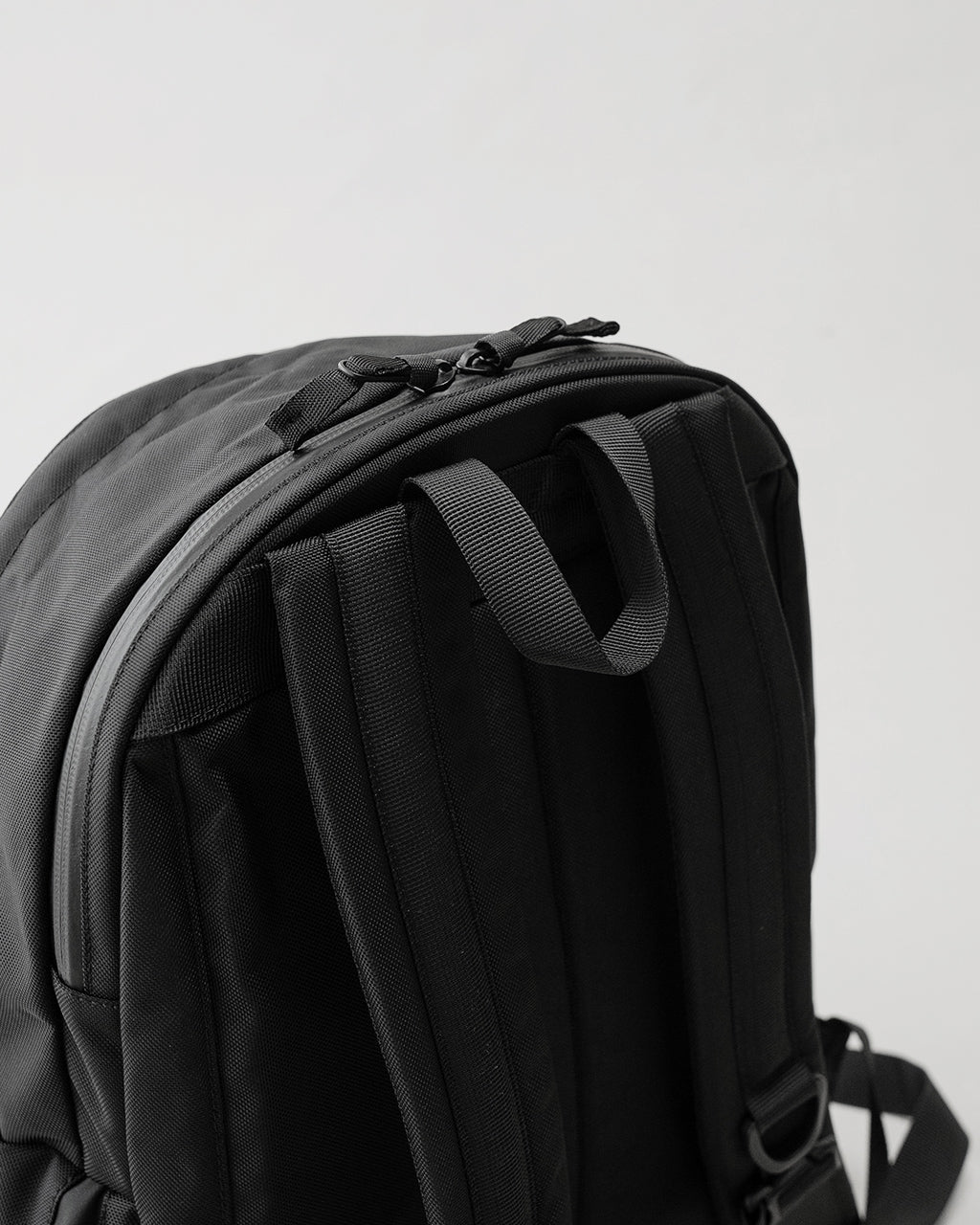 LC by LOWERCASE LC DAYPACK STANDARD 16Lの背面側ショット。黒系のバックパックで、肩紐とサイドのポケット部の縦リブが見える。耐久性のある生地とダブルファスナーの仕様がわかる画像。