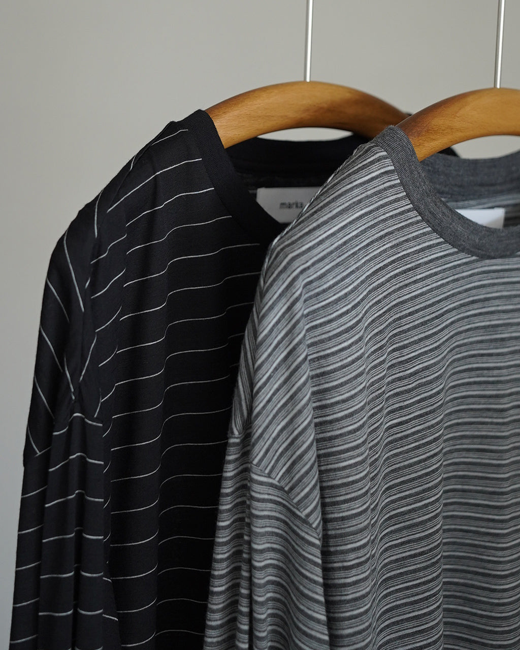 ブラック×ホワイトのボーダーとグレー系ボーダーの長袖Tシャツが掛けられ、首元のリブが際立つ様子。素材感のある生地と縦横のラインが落ち着いた印象を演出している前後ショット風のディスプレイ。