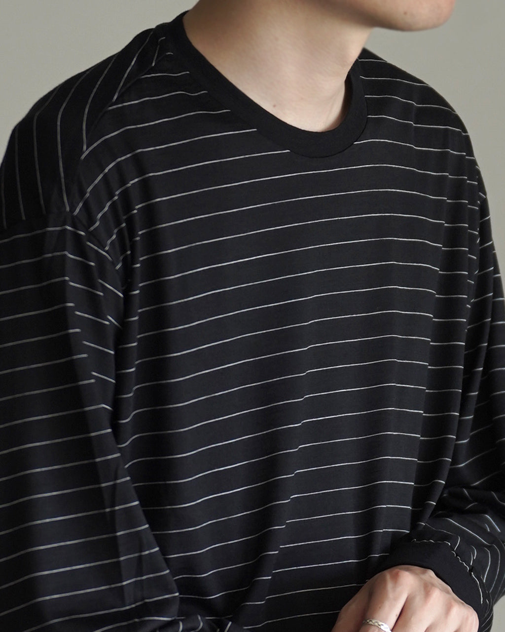 ブラック地に細い白いボーダーが入るクルーネック長袖Tシャツのアップ。袖口と裾リブが締まり、リラックス感のあるシルエットが特徴。