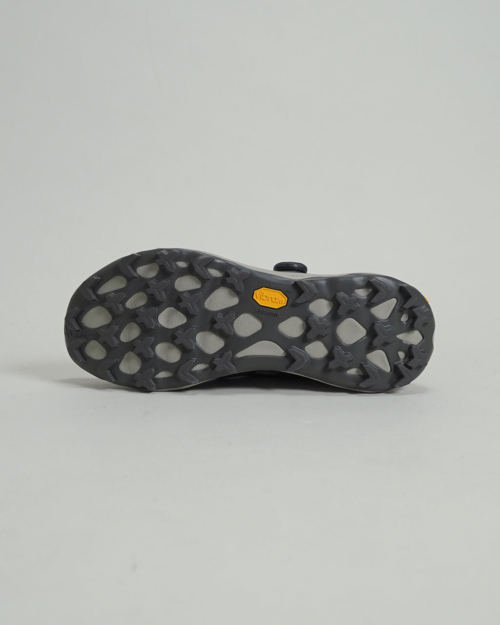 BOA式フィットのトレイルランニングシューズ、アッパーは通気性のある濃いグレー系、ソールにはVibram MegaGripの凹凸ラグが特徴。底面の接地パターンが視認できる写真。