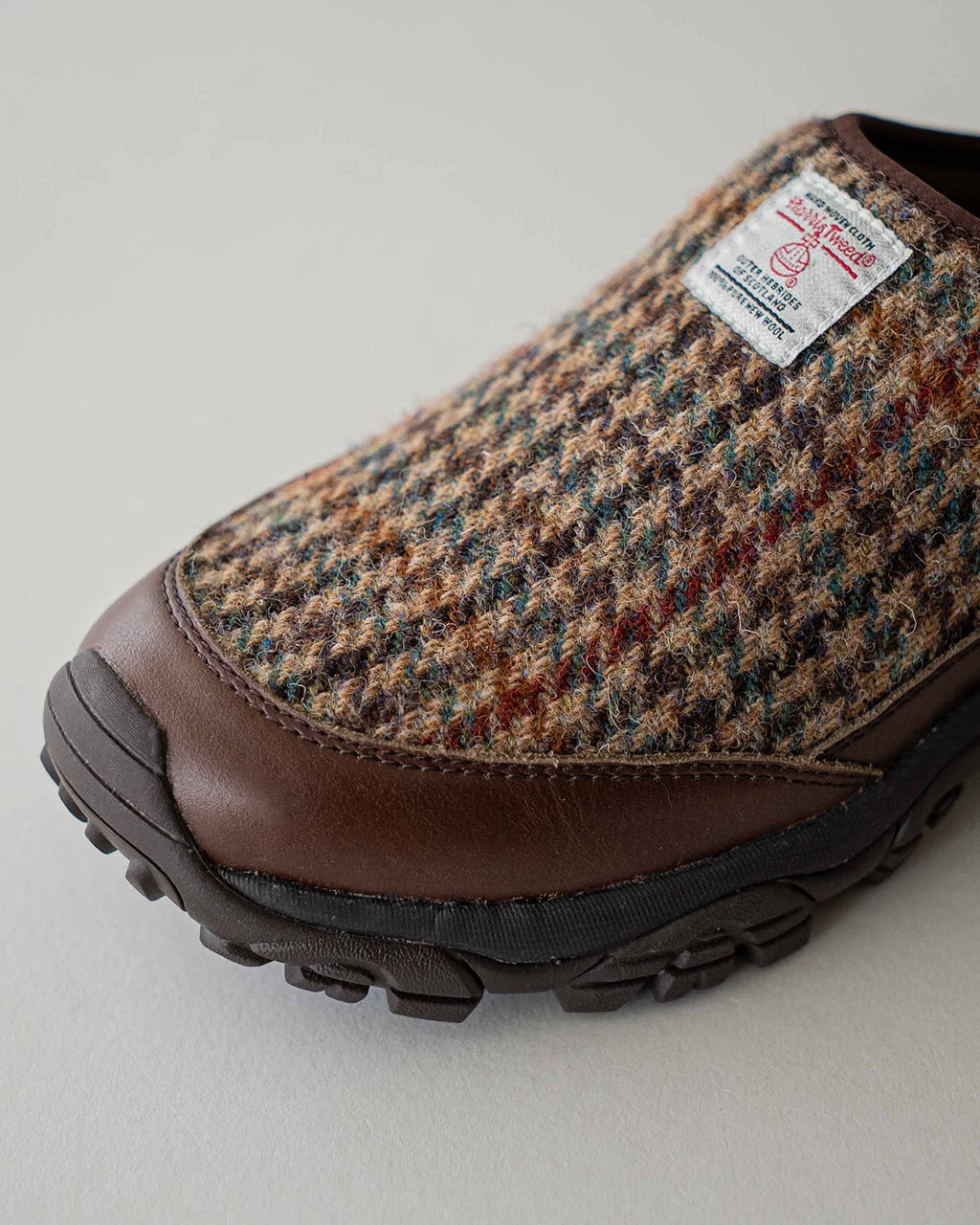Harris Tweedを配したつま先まで覆うキャップ風デザインのスリッポン。ウール混のチェック柄生地とブラウン レザーのアッパーが組み合わせられ、アウトソールは黒系カラーで耐久性を強調。
