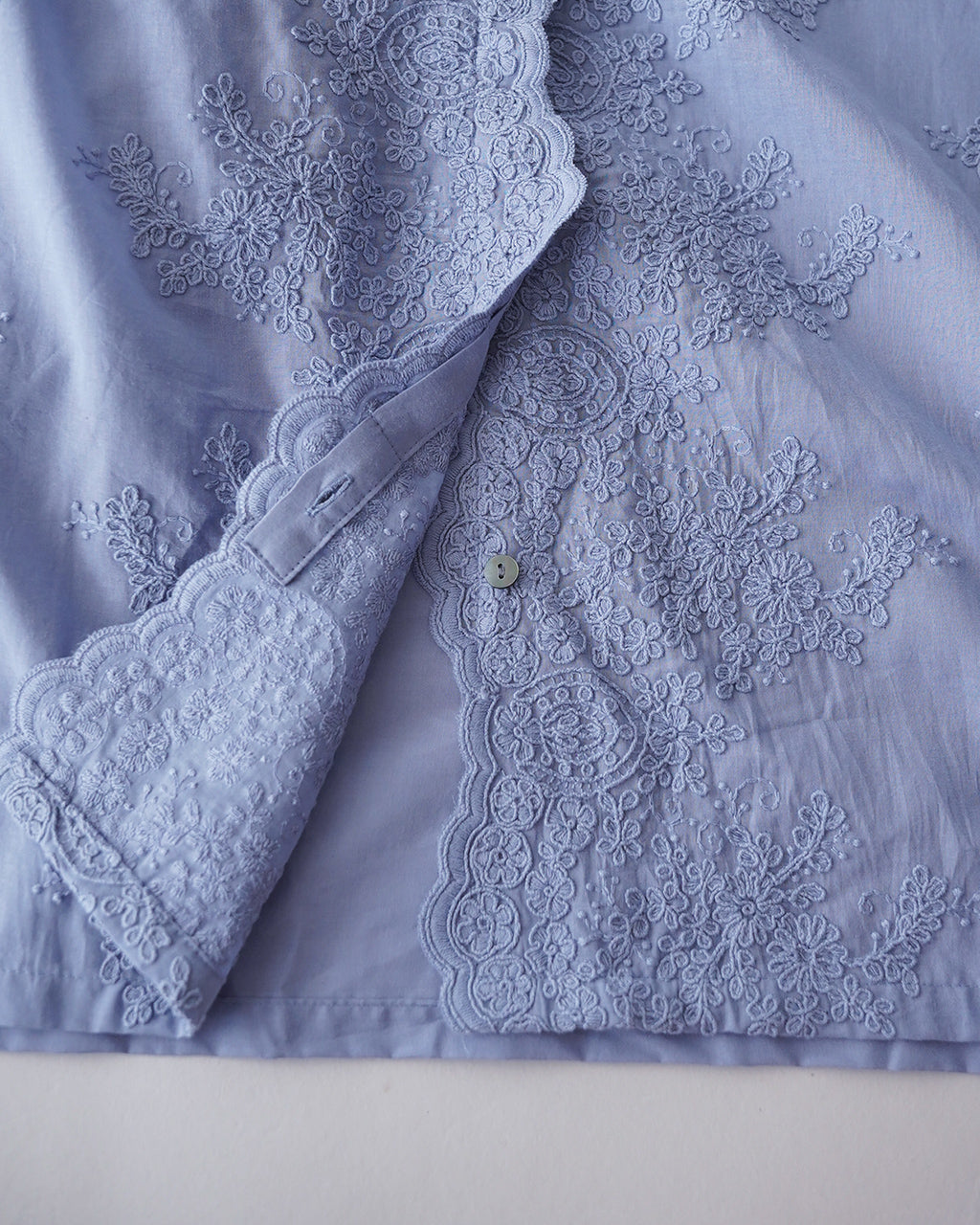 ミズイロインクのレース刺繍が施されたライトブルーの長袖シャツ。前立てと袖口に繊細なレースがあしらわれ、薄手の綿地が特徴的なディテールショット