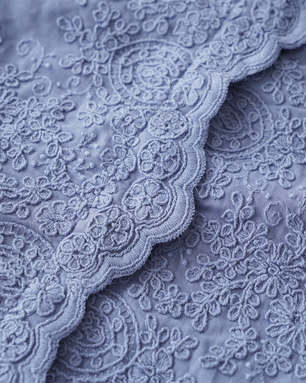 ブルー系レース生地のアップ。花柄の刺繍と繊細な縁取りが特徴の布地素材をクローズアップで示す
