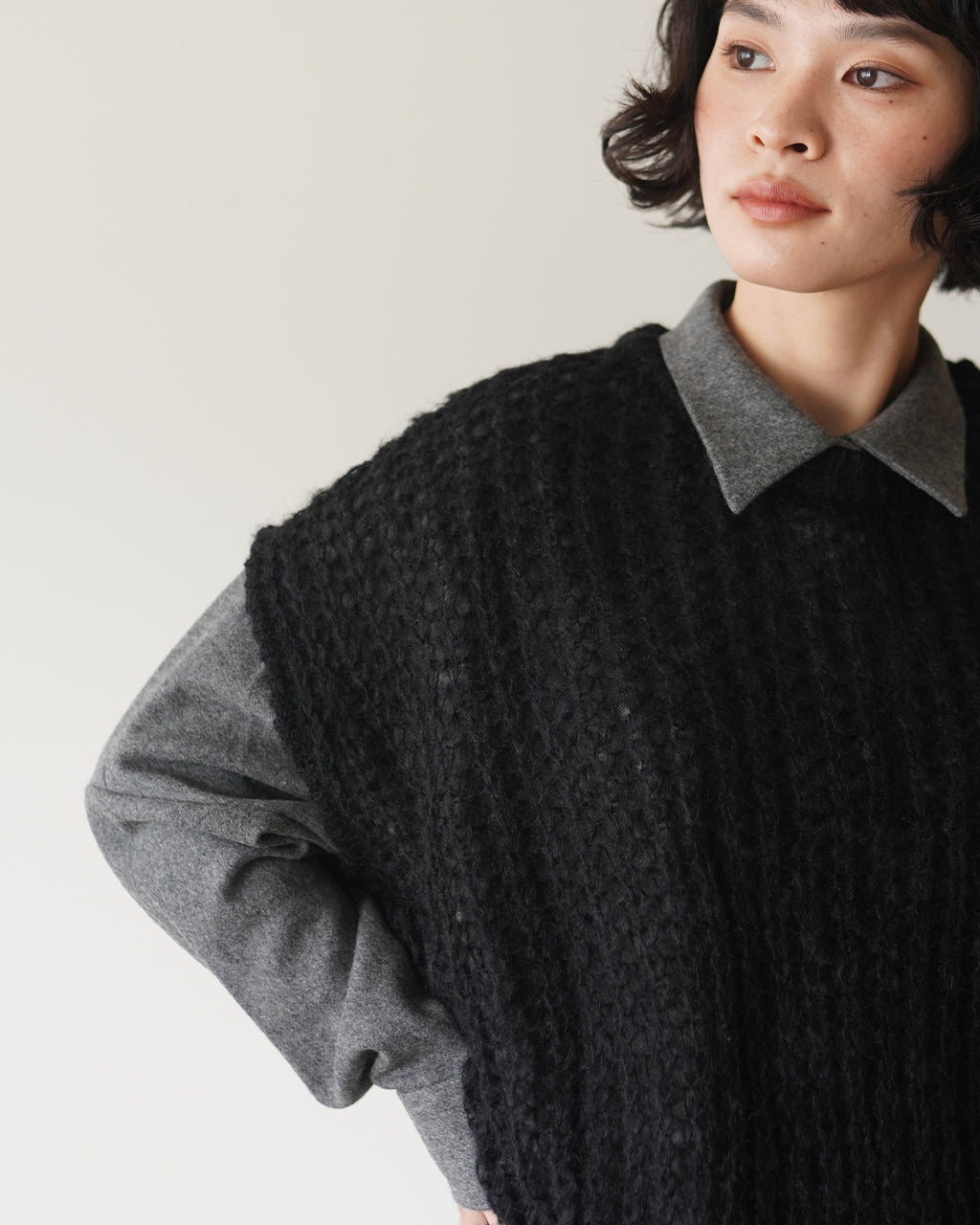 ミズイロインド hairly cocoon wide vestのディテールショット。黒のざっくり編みニットベストとグレーのシャツ地襟が重ねられ、立体感のある編み地が特徴的。