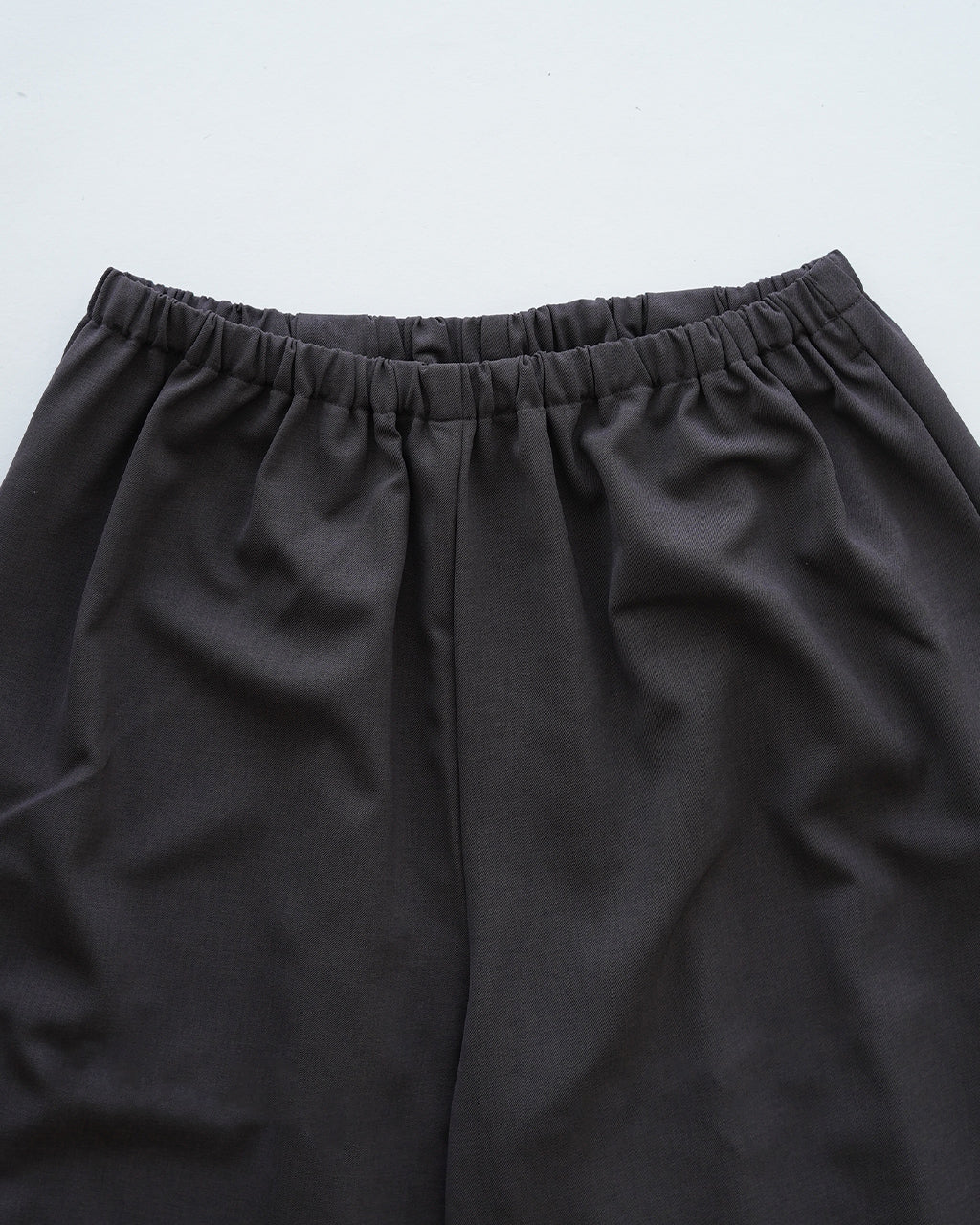 ウエストの幅広いゴムが特徴のパンツ。膝下まで落ち着いた雰囲気のワイドシルエットで、灰黒のカラーがシンプルながら品よく映える表情です。