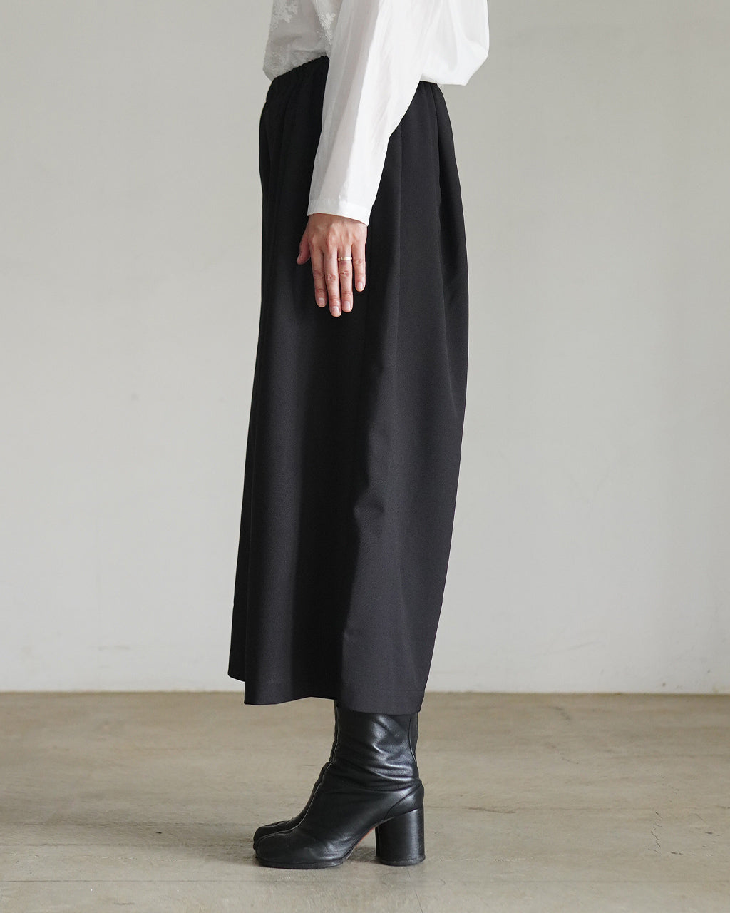 腰まわりがゆったりと落ち感のある黒のワイド半パンツ。白シャツを合わせた着用イメージで、ヒールブーツを合わせた全体のスタイルが視認できる横からのシルエット写真です。