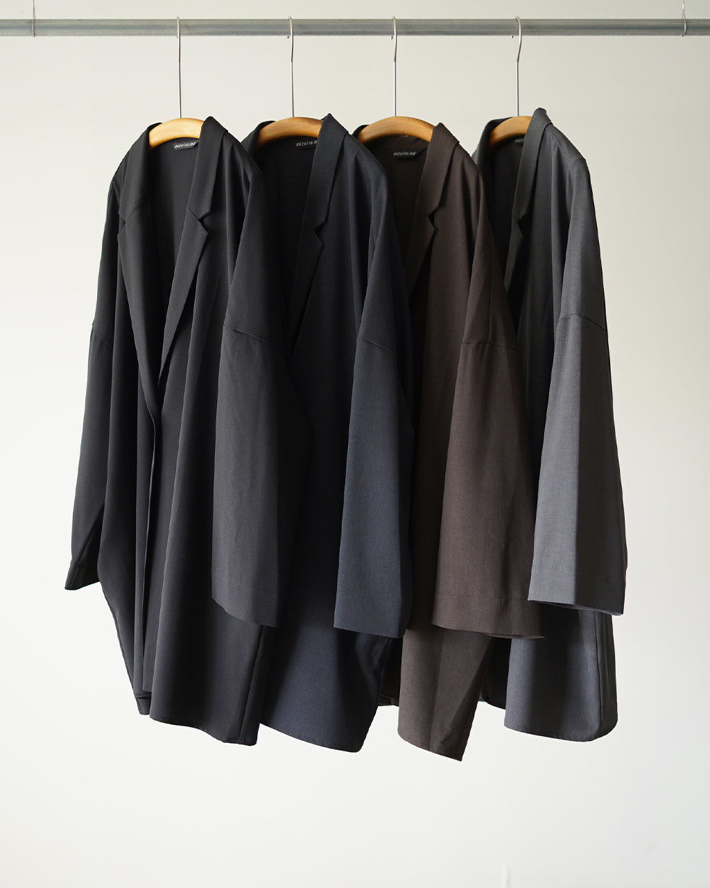 黒系のジャケットが複数枚並ぶディスプレイ。肩の落ちたビッグシルエットと長めの丈感が特徴的で、前を閉めたときの縦のラインが強調される佇まいを捉えた写真。