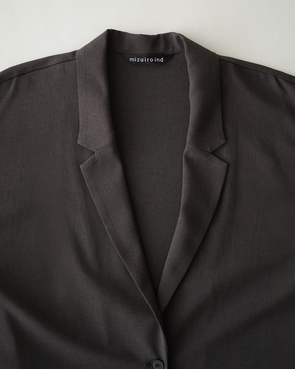 ミズイロインドのwide tailored shirt JK。深いブラウン系のジャケット風シャツを正面から捉え、ラペルと一列ボタンのミニマルなデザインが映えるショットです。